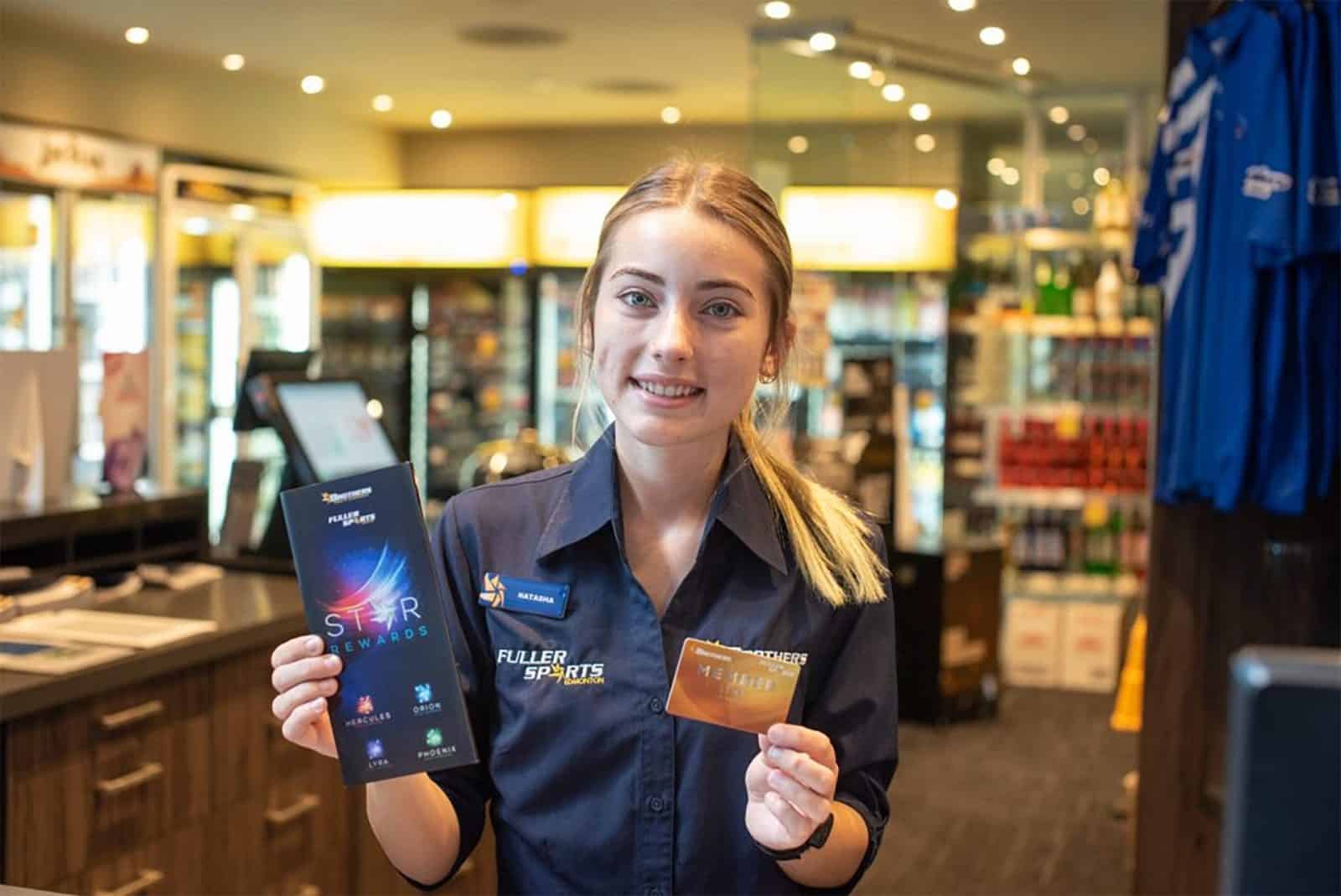 Smiling Brothers Leagues Club staff member standing indoors holding a card toward the camera.